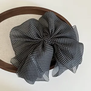 Detail of oversized black polka dot mesh bow hair claw clip on vintage wooden frame