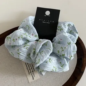 Detail of light blue floral scrunchie with white petals on branded black card packaging