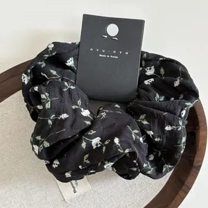 Detail of floral black scrunchie on wooden tray with Korean brand elegance label