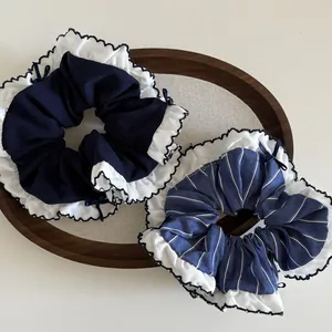 Detail of two navy blue scrunchies with white ruffles and small ribbon bows in a wooden tray