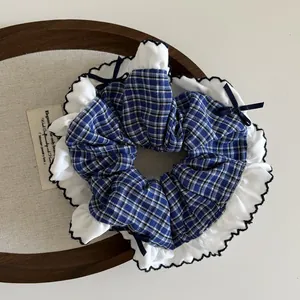 Detail of navy blue plaid scrunchie with white ruffled edges and small satin bows