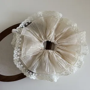 Detail of cream-colored oversized scrunchie with layered pleats and lace trim edges