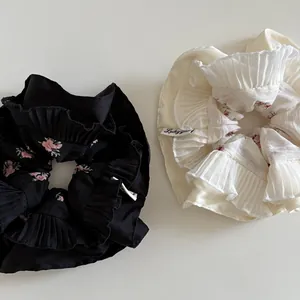 Close-up of pleated floral scrunchies in black and beige with delicate petal edges