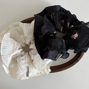 Close-up of pleated floral scrunchies in black and white with Lucky Girl woven label