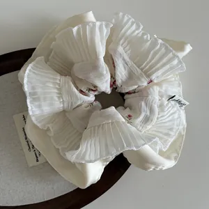 Close-up of ivory floral pleated scrunchie featuring a Lucky Girl woven label detail