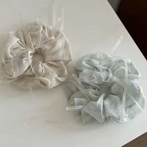 Gros plan de chouchous crème et bleu clair avec broderie de nœuds blancs et rubans