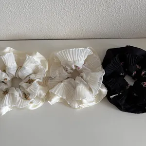 Three-piece set of pleated floral scrunchies in beige, white, and black chiffon fabric