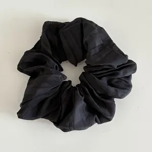 Detail of black striped fabric scrunchie with pleated texture and elastic inner band