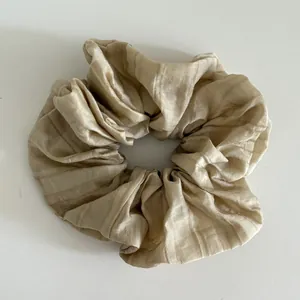 Detail of champagne pleated fabric hair scrunchie with vertical textured sheer fabric