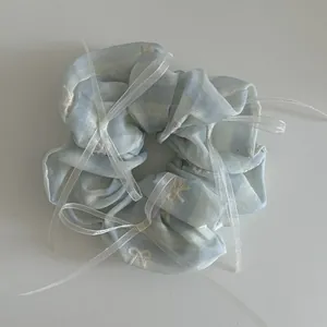Détail du chouchou rayé bleu clair avec nœuds en ruban blanc et texture en organza