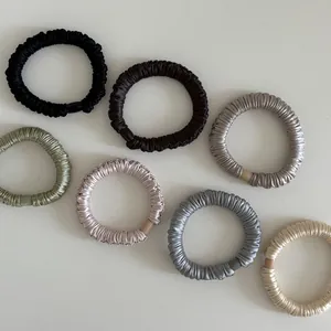 Close-up of seven assorted satin scrunchies showing glossy silk texture and pleated detail