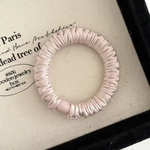 Detail of champagne pleated satin scrunchie with matte pink bead in a display box