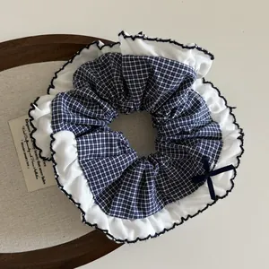 Blue plaid scrunchie with white ruffled edges and a navy bow hair accessory