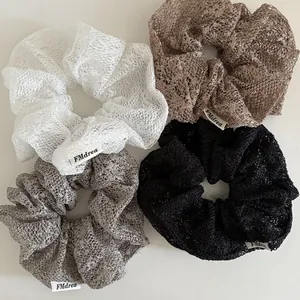 Detailset aus vier Spitzen-Scrunchies in Weiß, Beige, Grau und Schwarz mit Webetiketten