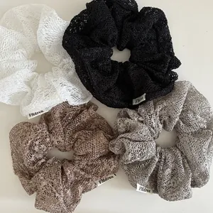 Detailaufnahme von vier Spitzen-Haargummis in Weiß, Schwarz, Braun und Grau mit Markenetikett