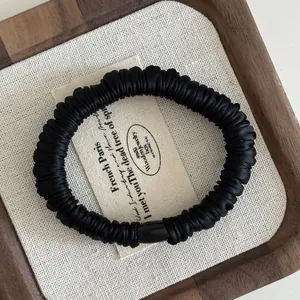 Detail of black pleated satin hair tie with smooth oval bead on elegant canvas texture