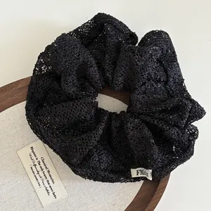 Detail eines schwarzen Spitzen-Scrunchies mit Stickerei und gewebtem Logo-Etikett