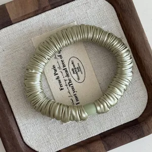 Detailed close-up of a sage green satin pleated hair scrunchie on a wooden tray