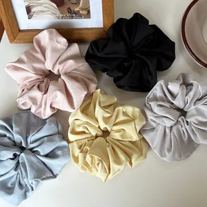 Close-up of five oversized scrunchies in cream, blue, and grey with soft pleated fabric