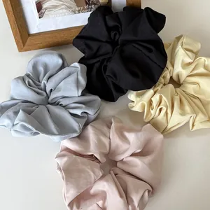 Detailed view of oversized satin scrunchies in four muted colors on a minimal background