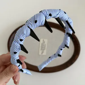 Detail shot of a blue and white striped wavy headband with black spiked punk accents