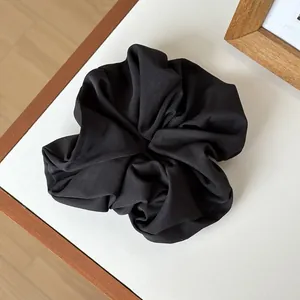 Macro shot of oversized matte black scrunchie showing detailed fabric pleats and texture