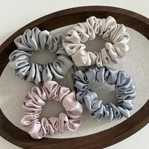 Macro detail of four satin silk scrunchies in gray, champagne, pink, and blue on a tray