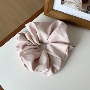 Close-up of a soft pink satin scrunchie with a glossy silk texture and elegant folds