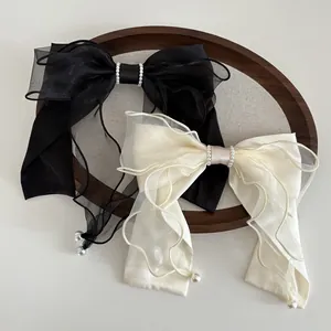 Detailed view of satin and organza bow hair clips with elegant pearl charms in black and white