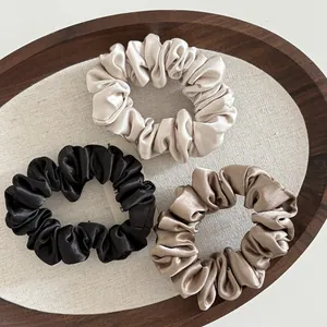 Close-up of three satin scrunchies in cream, black, and brown colors on a wooden tray