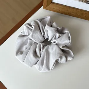 Detail view of large light gray scrunchie with soft glossy fabric texture on beige background