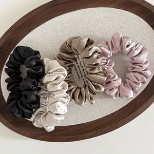 Close-up of four satin scrunchies in black, beige, bronze, and pink on a wooden tray
