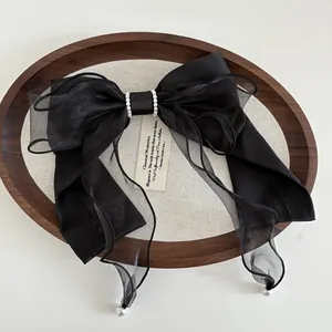 Detail of a large black satin bow hair clip with layered mesh and elegant pearl accents