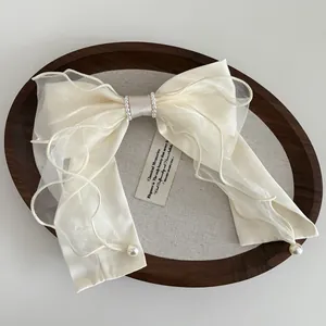 Detail of cream satin and organza bow hair clip with faux pearl trim and elegant long streamers