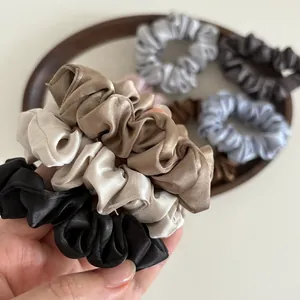 Detailed shot of pleated satin scrunchies set in neutral tones with silky glossy texture