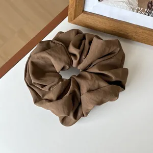 Detail view of a large coffee brown pleated scrunchie with subtle luster on white desk