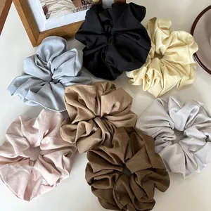 Seven oversized matte fabric scrunchies in minimalist colors on a white surface