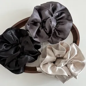 Three-piece satin scrunchies set in black, grey, and champagne on a wooden tray
