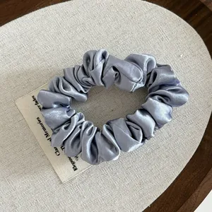Macro detail of silver satin scrunchie with pearl sheen on a wooden tray setting
