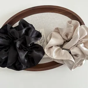 Detailed texture of ivory and black premium satin silk hair scrunchies on a wooden tray