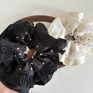 Close-up of polka dot satin scrunchies with pleated ruffle edges in black and cream