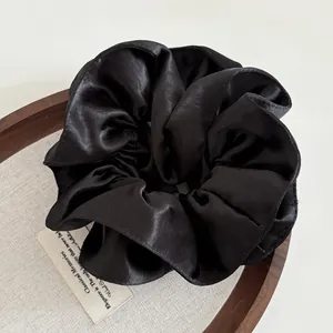 Detailed view of premium black satin scrunchie with elegant pleated silk texture on a wooden tray