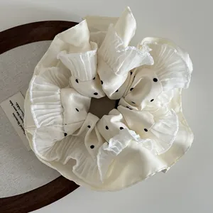 Close-up of cream polka dot scrunchie with layered ruffle edges on vintage tray