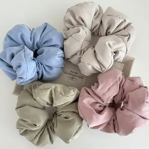 Detail of four matte satin scrunchies in pastel tones on a minimalist linen box tray