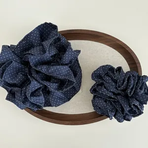 Dettaglio di scrunchie a pois blu navy in due dimensioni su un vassoio di legno