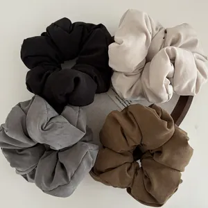 Detail of four matte cotton hair scrunchies in neutral colors on a round grey tray