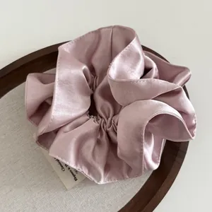 Macro detail of a high-quality heavy satin scrunchie in elegant dusty pink on a wooden tray