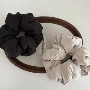 Detail of oversized cloud hair scrunchies in black and beige fabric on a wooden tray