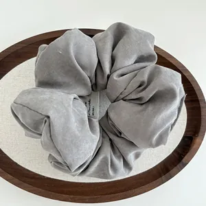 Close-up of a large grey cotton scrunchie with soft fabric texture on a wooden tray