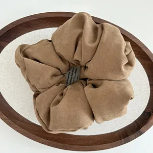 Close-up of a large brown plush scrunchie with soft fabric folds and a brand logo tag